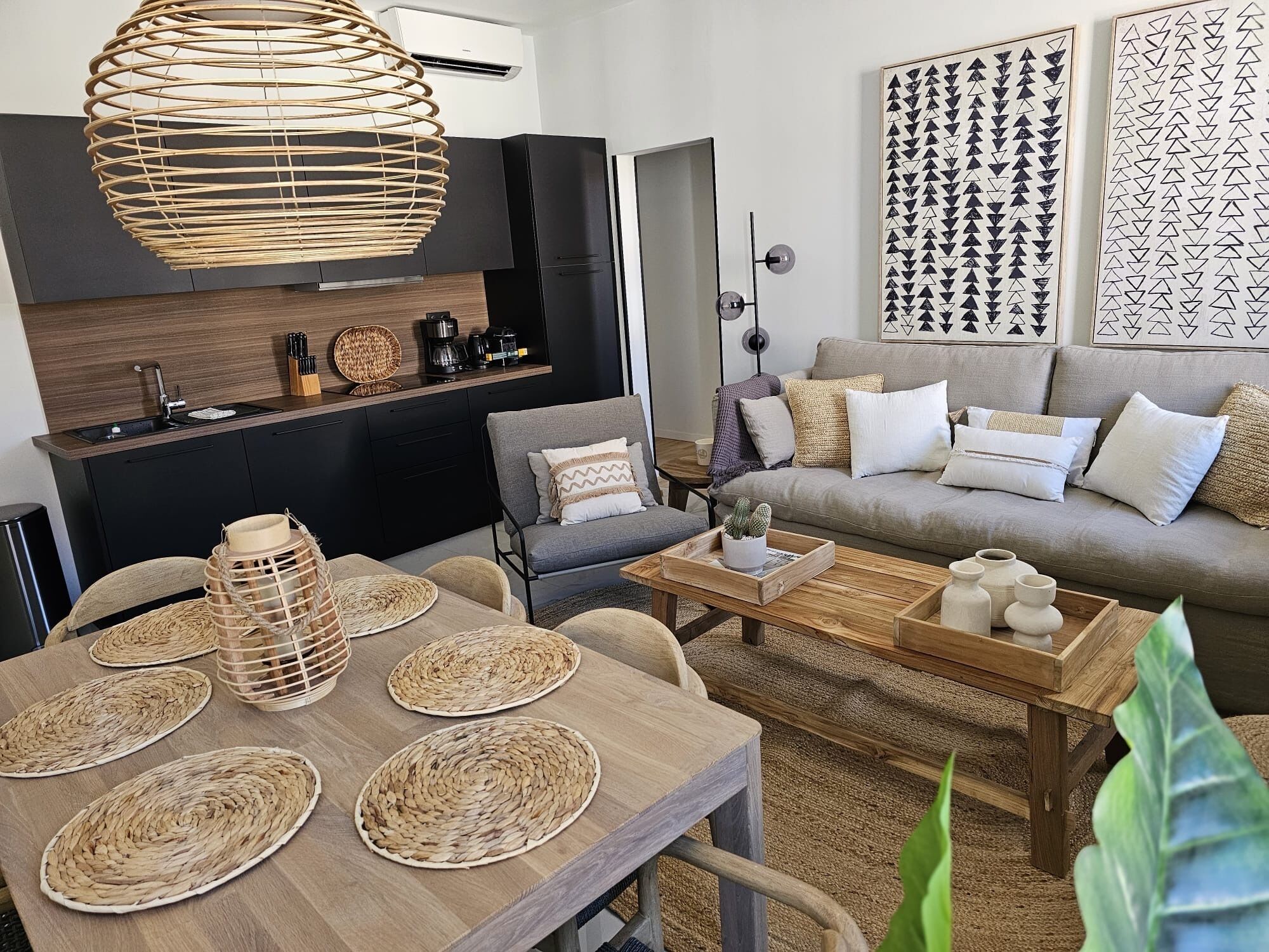 A modern living room with a dining area, featuring a woven light fixture, a sofa with cushions, and a coffee table with decorative items.