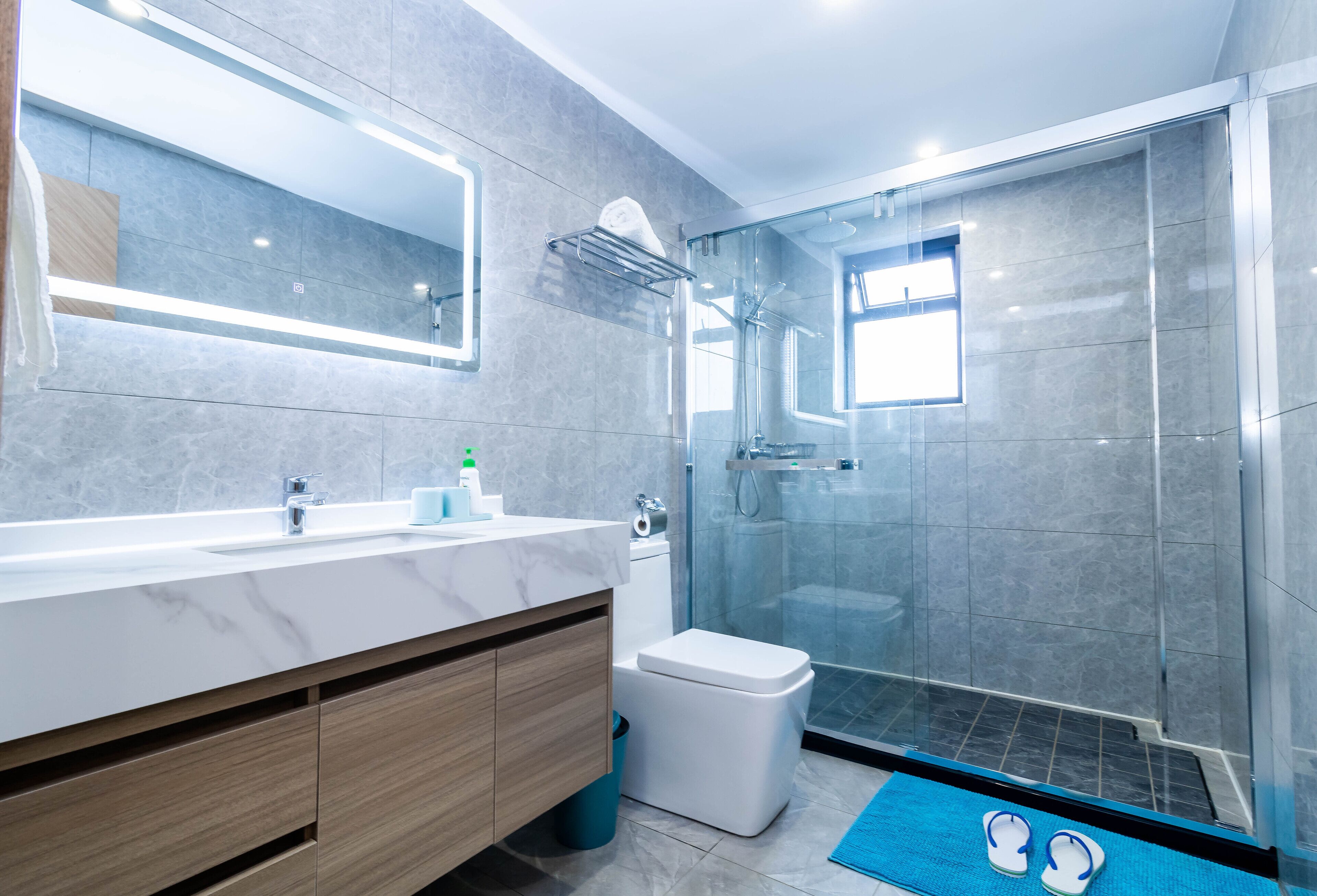 Un baño moderno con tocador de mármol, cabina de ducha de vidrio y alfombra de baño azul.