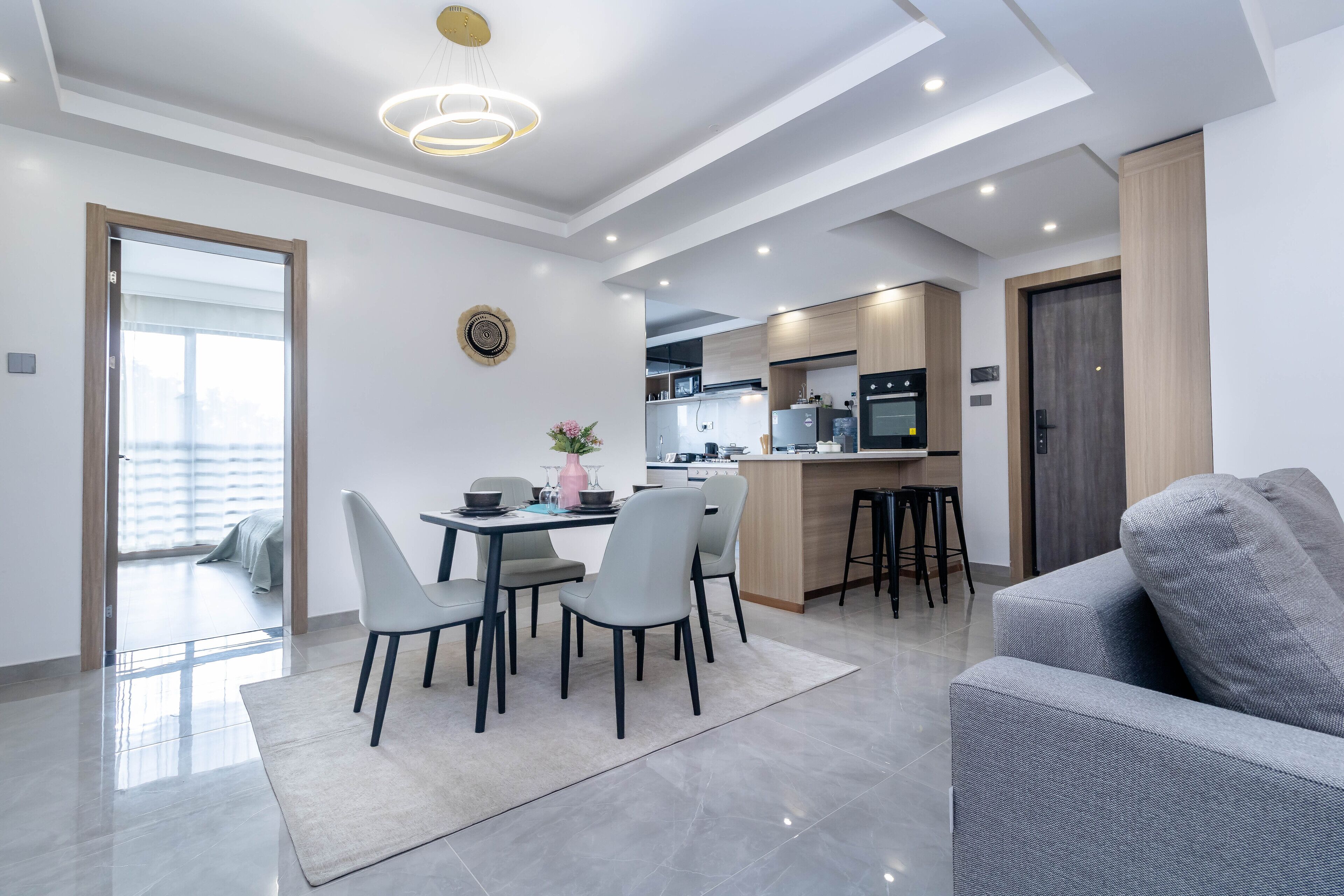 A modern living room with a grey sofa, a dining table with chairs, and a kitchen area in the background.
