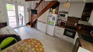 A kitchen with white cabinets, a wooden staircase, a dining area with a table, and a view through a glass door.