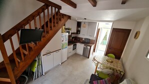 A kitchen with wooden beams, a dining area with a table and chairs, and a staircase. - Maisonnette du Clos - Avec piscine partagée (Argeles-sur-Mer)