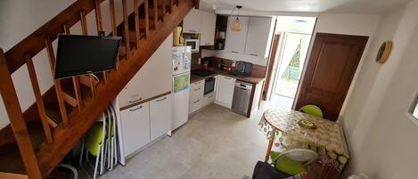 Una cocina con vigas de madera, un comedor con mesa y sillas, y una escalera.