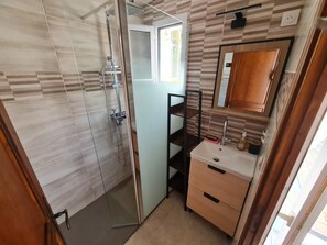 A bathroom with a glass shower enclosure, a sink with a mirror, and a wooden cabinet. - Maisonnette du Clos - Avec piscine partagée (Argeles-sur-Mer)