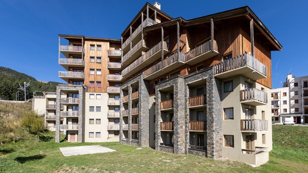 Un hotel de varios pisos con balcones, fachada de piedra y madera, y un patio con césped.