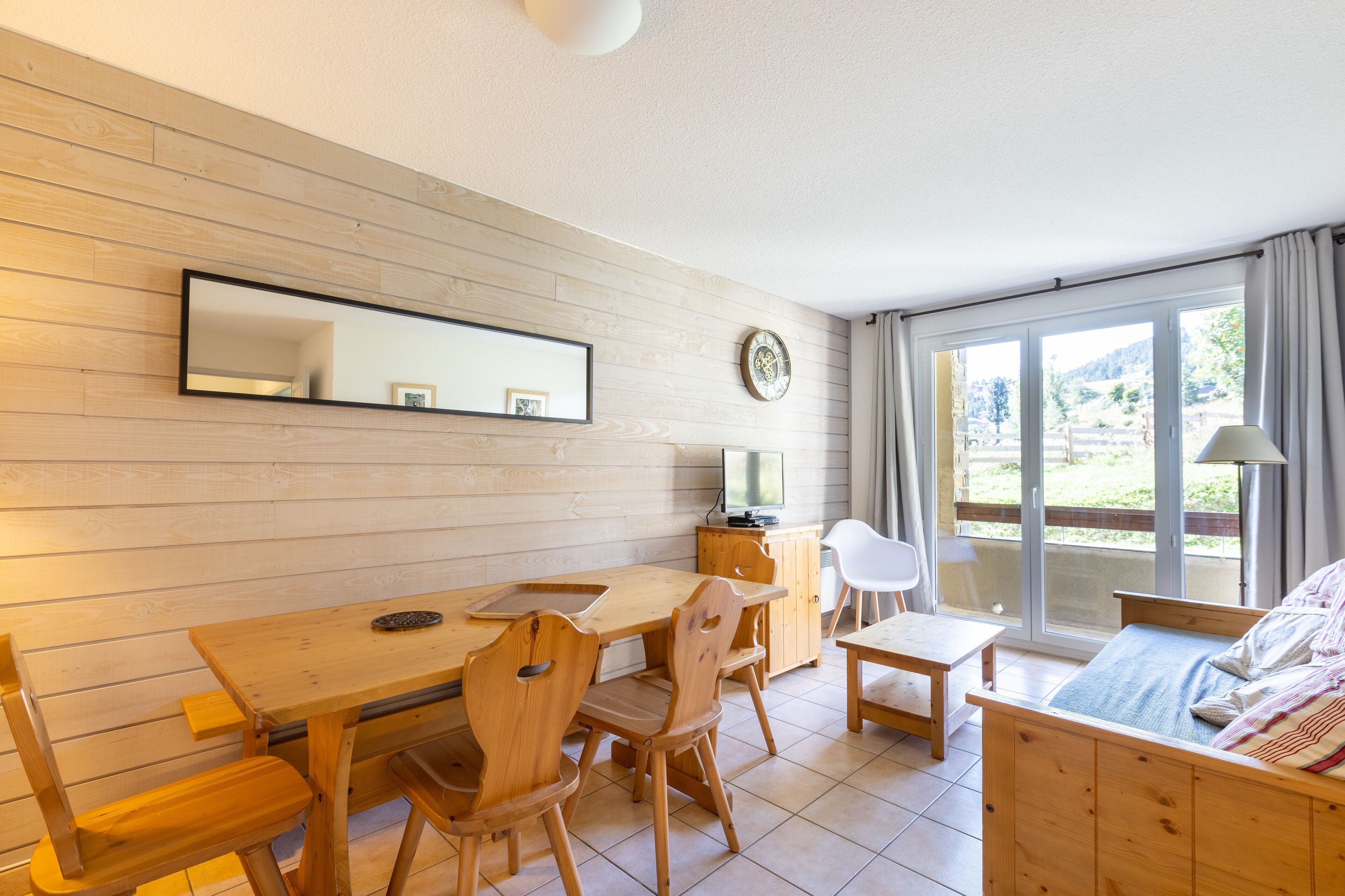 Une pièce comprenant une table à manger en bois, des chaises, un lit, un téléviseur et une grande fenêtre donnant sur l’extérieur.