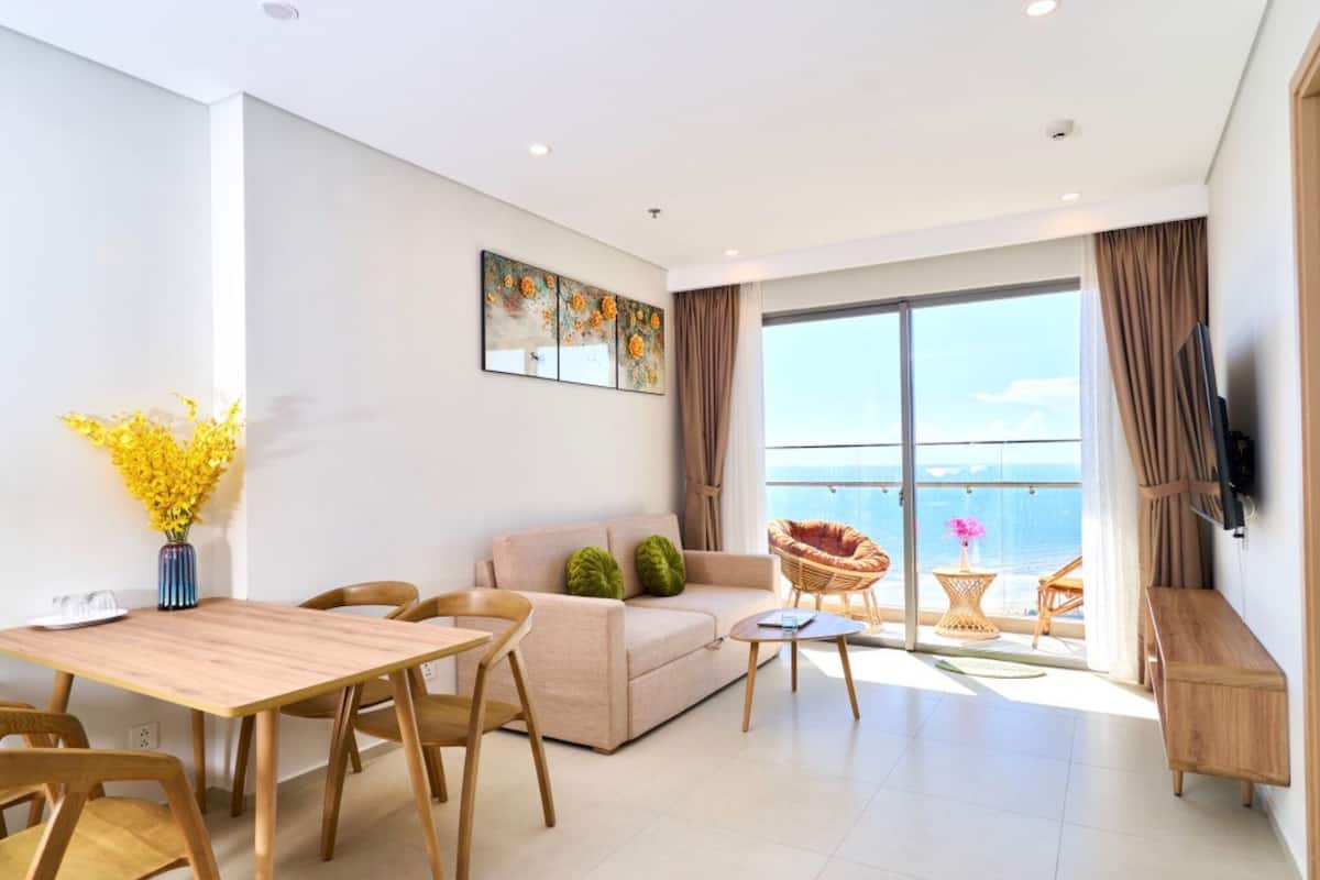 Un salon moderne avec un canapé, une table à manger et des chaises. Une grande fenêtre offre une vue sur la mer.