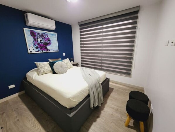Ein Schlafzimmer mit einem Bett, einem Fenster mit Jalousien, einem Bild an der Wand und einer Klimaanlage.