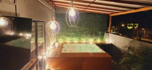 Ein moderner Außenbereich mit Whirlpool, Holzboden, einer grünen Wand und Pendelleuchten.