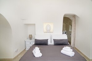 A hotel room with a large bed, two pillows, a nightstand with a lamp, a framed artwork above the bed, and towels on the floor. - trullo lantane by Pugliadamre (San Michele Salentino)