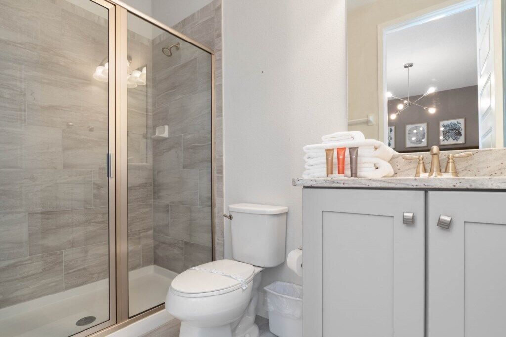 Een moderne badkamer met een douchecabine van glas, een wit toilet en een wastafel met een marmeren aanrechtblad.