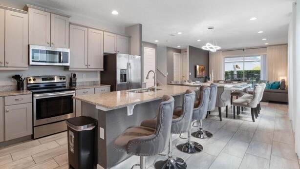 A modern kitchen with stainless steel appliances, a central island with bar stools, and a dining area with a large window.