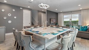 A modern dining room with a central island, grey walls, and a view of the outdoors.