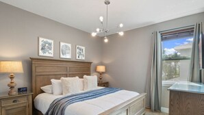 Un dormitorio con una cama, lámparas de noche, un reloj, obras de arte enmarcadas, una lámpara de techo y una ventana con cortinas.