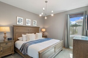Una camera da letto con un letto, abat-jour, una sveglia, opere d'arte incorniciate, un lampadario a soffitto e una finestra con tende.