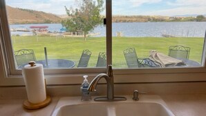 Un évier de cuisine donnant sur un lac, avec des chaises et une table à l’extérieur.