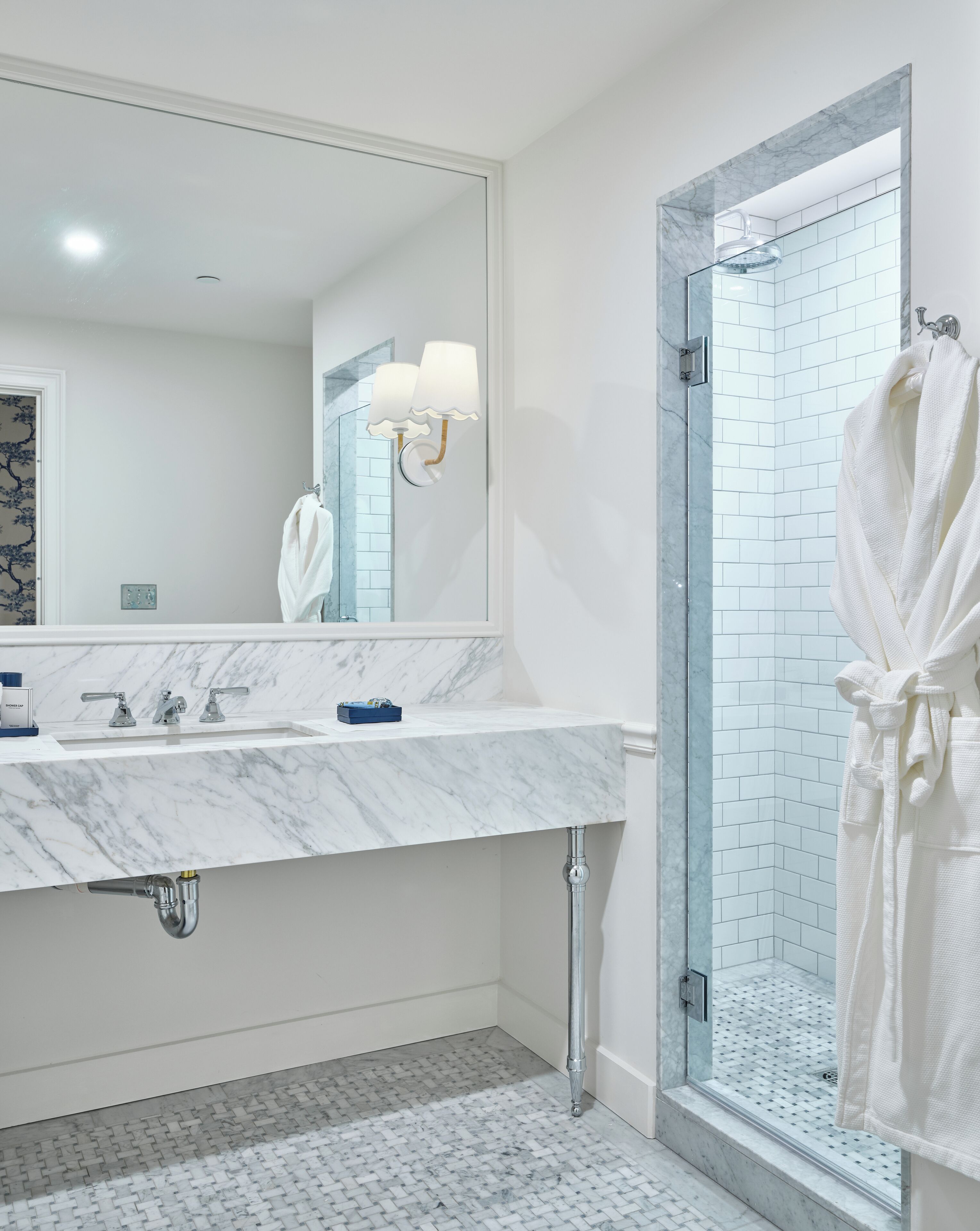 A modern bathroom with a marble sink, a glass-enclosed shower, and a white bathrobe hanging on the door.