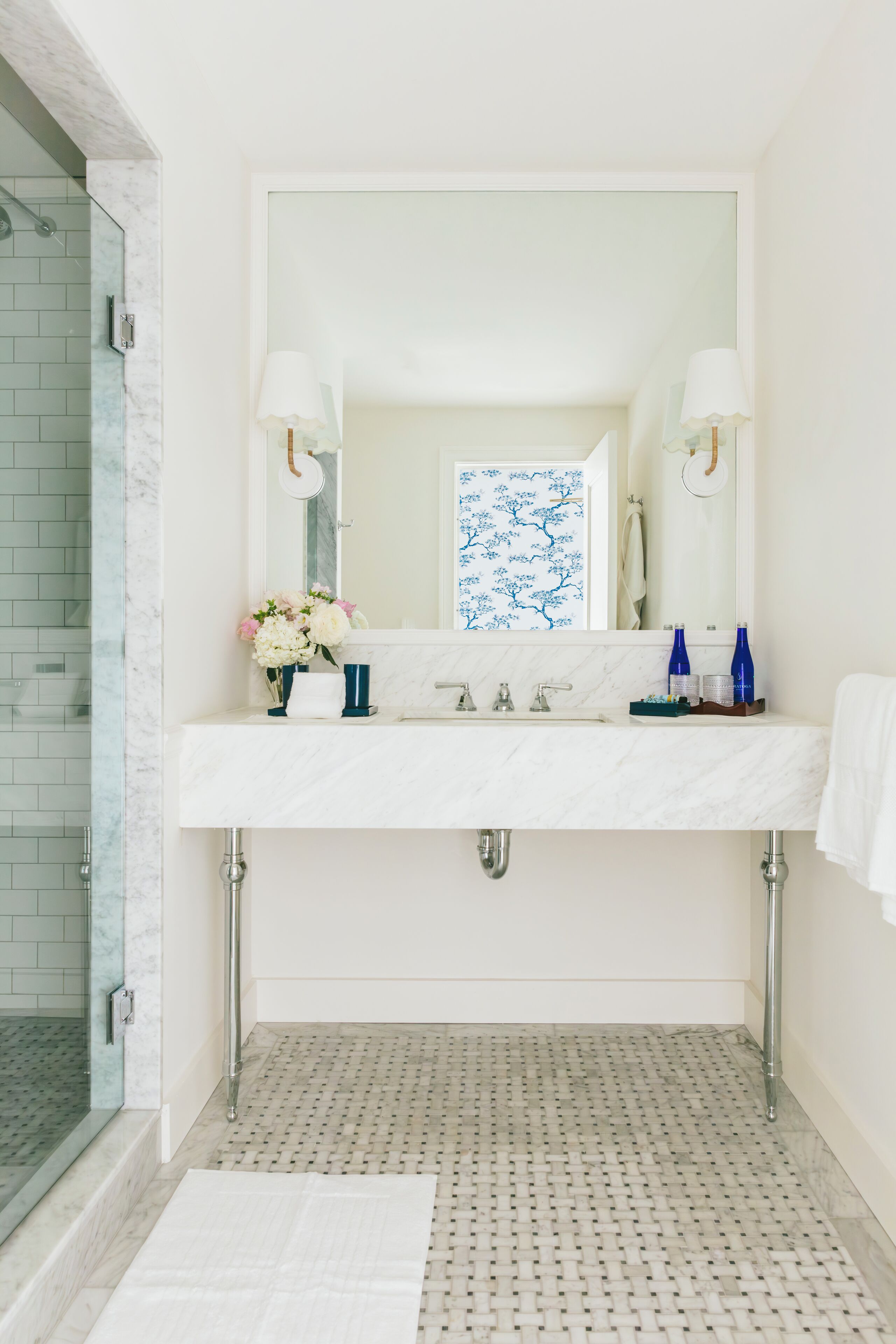 Un bagno con un lavabo in marmo bianco, due rubinetti, uno specchio grande e una cabina doccia con porta in vetro.