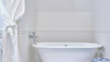 Une salle de bain avec une baignoire sur pieds, un peignoir blanc accroché à un porte-serviettes, un tapis de bain blanc, un petit objet décoratif et un vase bleu et blanc.
