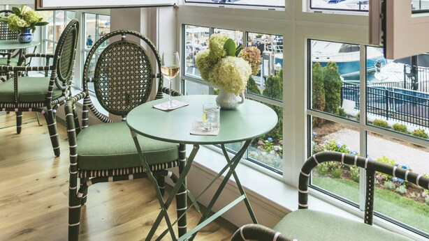 Una habitación con ventanas amplias, una mesa redonda y sillas tapizadas en verde.