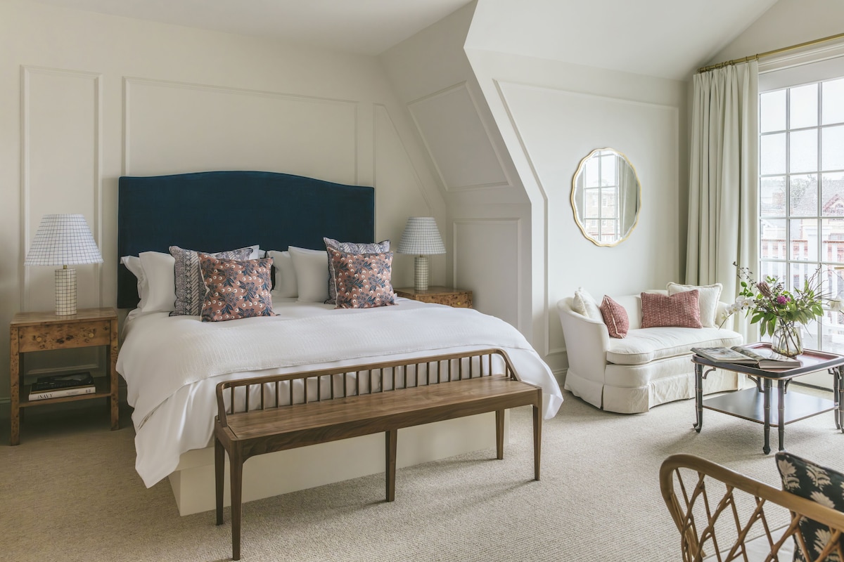 A bedroom with a large bed, a bench, a sofa, a coffee table, and a mirror.