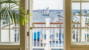 Vista desde una habitación con un amplio ventanal que da a un puerto deportivo con veleros e yates amarrados.
