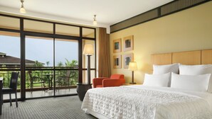 Habitación de hotel con una cama grande, un balcón con sillas y vistas a zonas verdes.