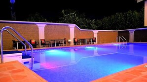Una piscina exterior con solárium de baldosas, una escalera y varias sillas alrededor.