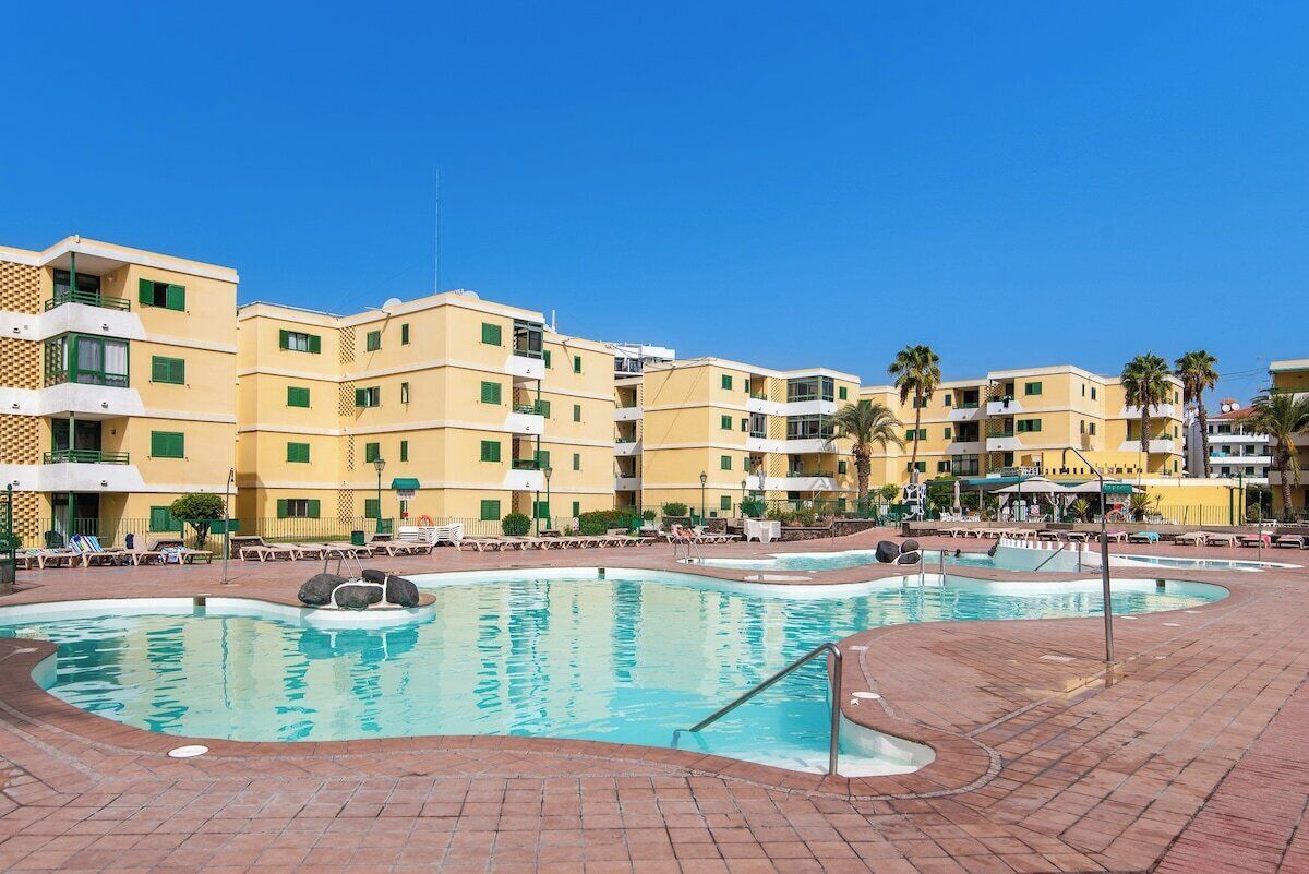 A hotel with a swimming pool, multiple balconies, and a clear blue sky.