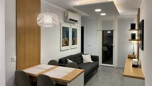 A modern living space with a dining area, a sofa, a TV, and an air conditioning unit.