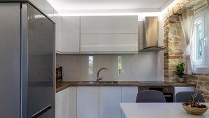 Eine kleine Küche mit Edelstahlkühlschrank, weißen Schränken, einer Holzausziehtafel, einer Spüle und einem Essbereich mit Tisch und Stühlen.