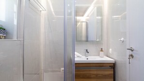 Ein modernes Badezimmer mit Duschkabine aus Glas, einem weißen Waschbecken mit Holzschrank und einem Spiegel darüber.