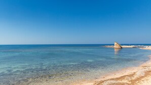 A beach with clear water, a sandy shore, and a stone structure in the distance. - 3386 Un Sogno sul Mare by Barbarhouse (Salve)