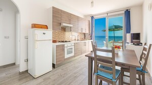 A modern kitchen with a view of the sea, a dining area with wooden furniture, and a TV on a cabinet. - 3386 Un Sogno sul Mare by Barbarhouse (Salve)