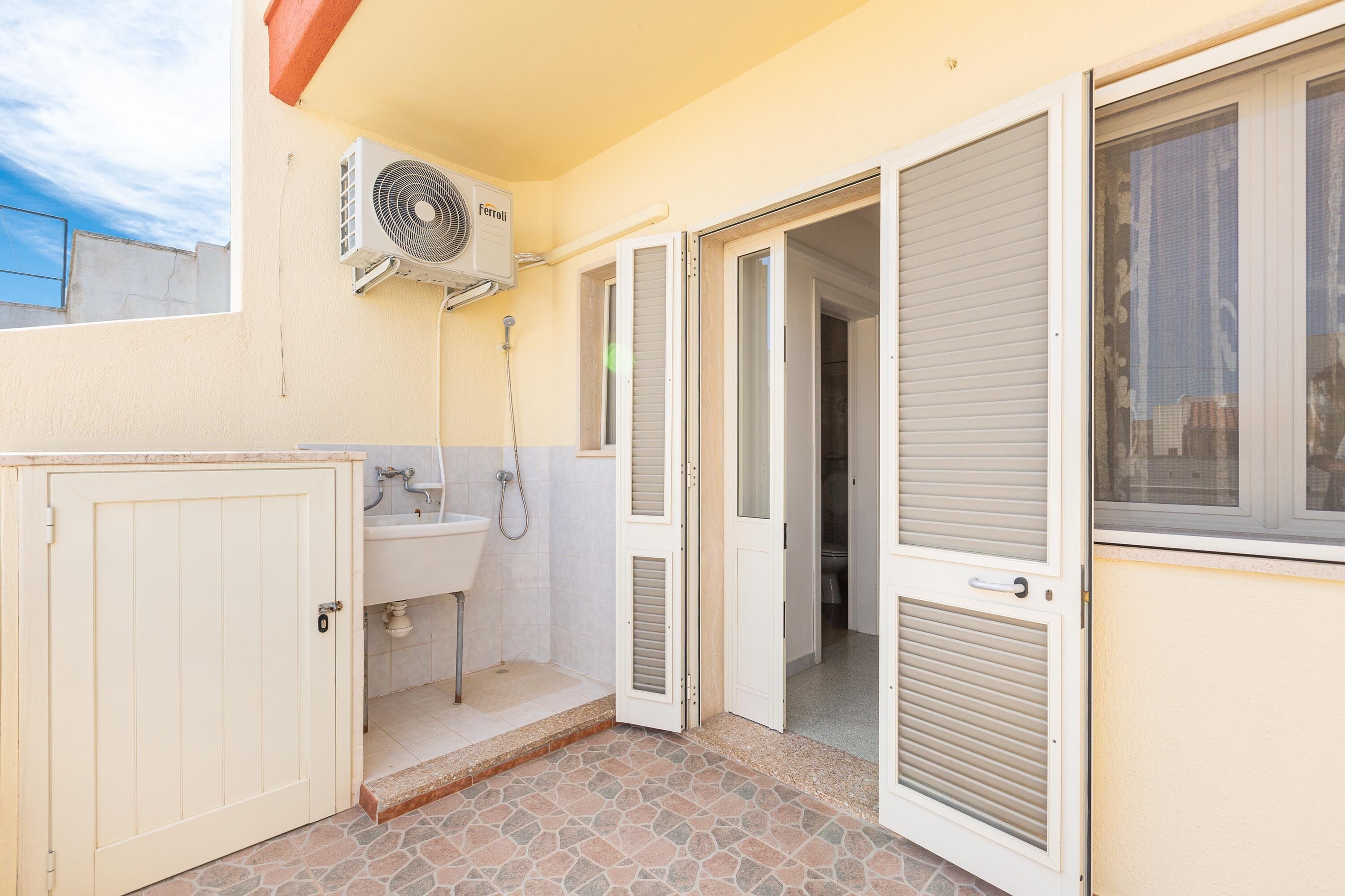 A compact bathroom with a sink, a shower, and a fan mounted on the wall.