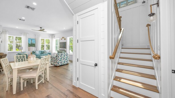 A spacious living room with a dining area, a staircase with a rope handrail, and a view of the outdoors through large windows. - Located in Captiva Village! Beautifully Designed Pool Home (Captiva)