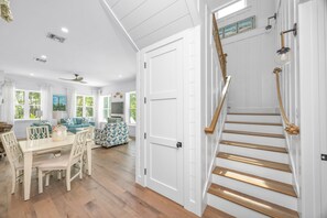 A spacious living room with a dining area, a staircase with a rope handrail, and a view of the outdoors through large windows. - Located in Captiva Village! Beautifully Designed Pool Home (Captiva)