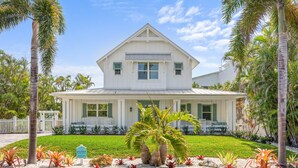 A two-story white house with a gabled roof, a covered porch, and a well-maintained lawn with tropical plants. - Located in Captiva Village! Beautifully Designed Pool Home (Captiva)