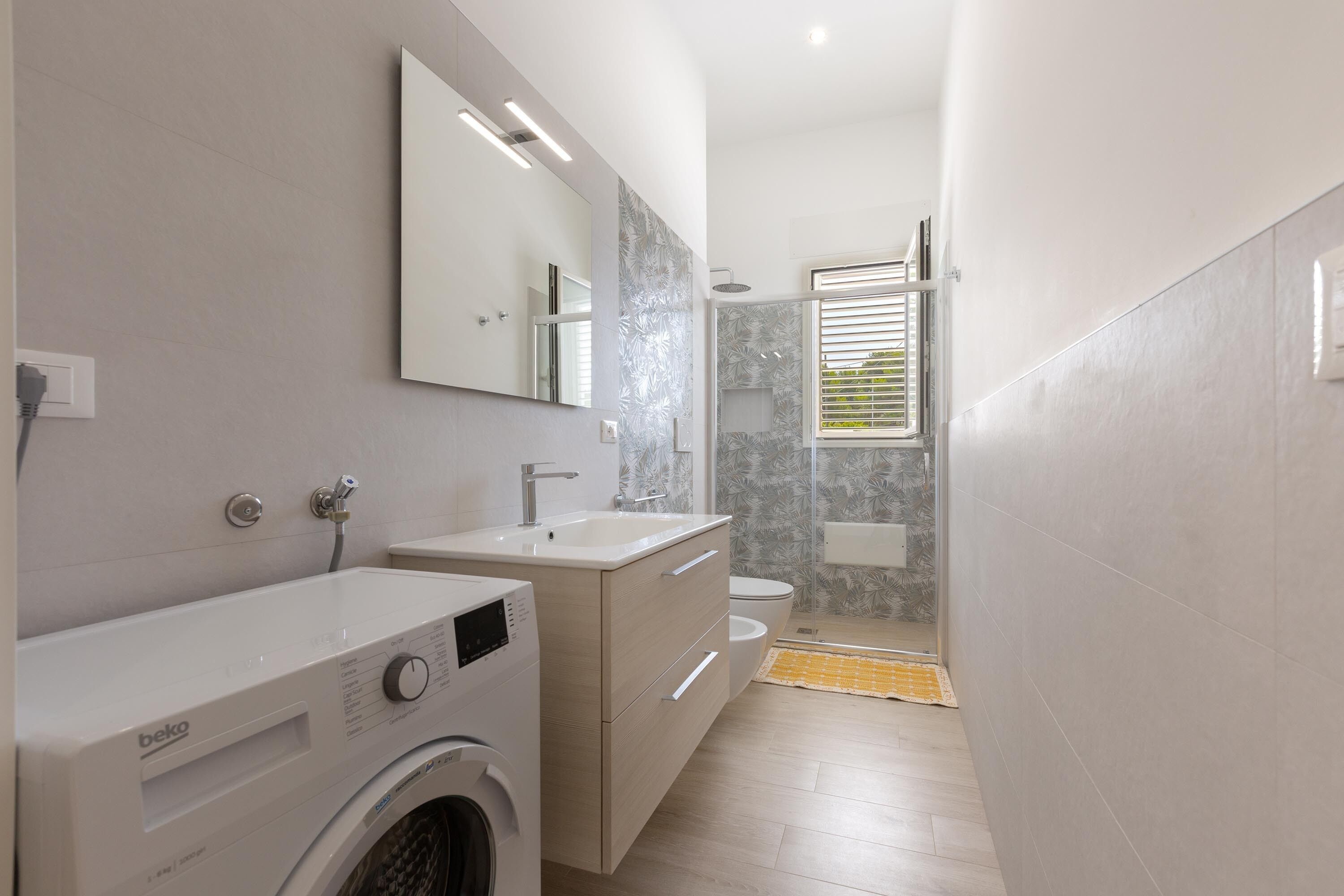 A modern bathroom with a washing machine, a sink, and a toilet.