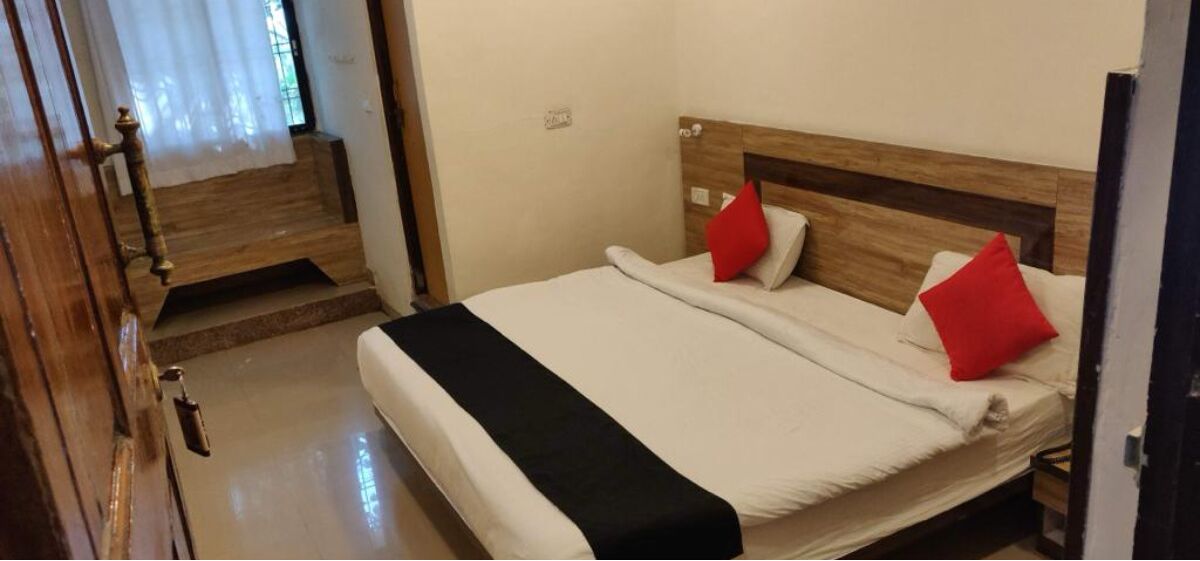 Habitació d'hotel amb un capçal de llit de fusta, un llit amb roba de llit blanca i dos coixins vermells, i una manta negra.