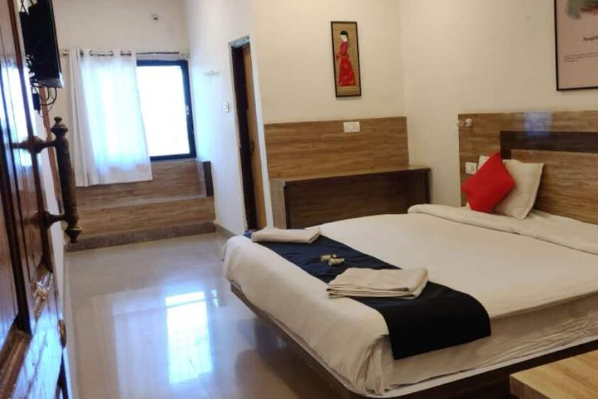 Une chambre d’hôtel avec un grand lit, une tête de lit en bois et une fenêtre avec des rideaux.