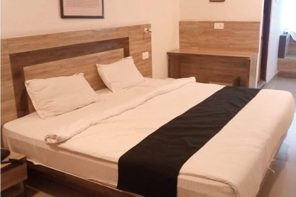 Un lit bien fait, avec une tête de lit et un pied de lit en bois, un tableau encadré accroché au mur et un appareil de climatisation placé au-dessus du lit.
