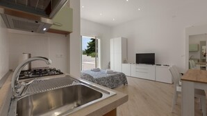 A modern kitchen with a stainless steel sink, a gas stove, and a dining area with a wooden table and chairs. - 3545 Antonio - App Pulcinella by Barbarhouse (Castrignano del Capo)