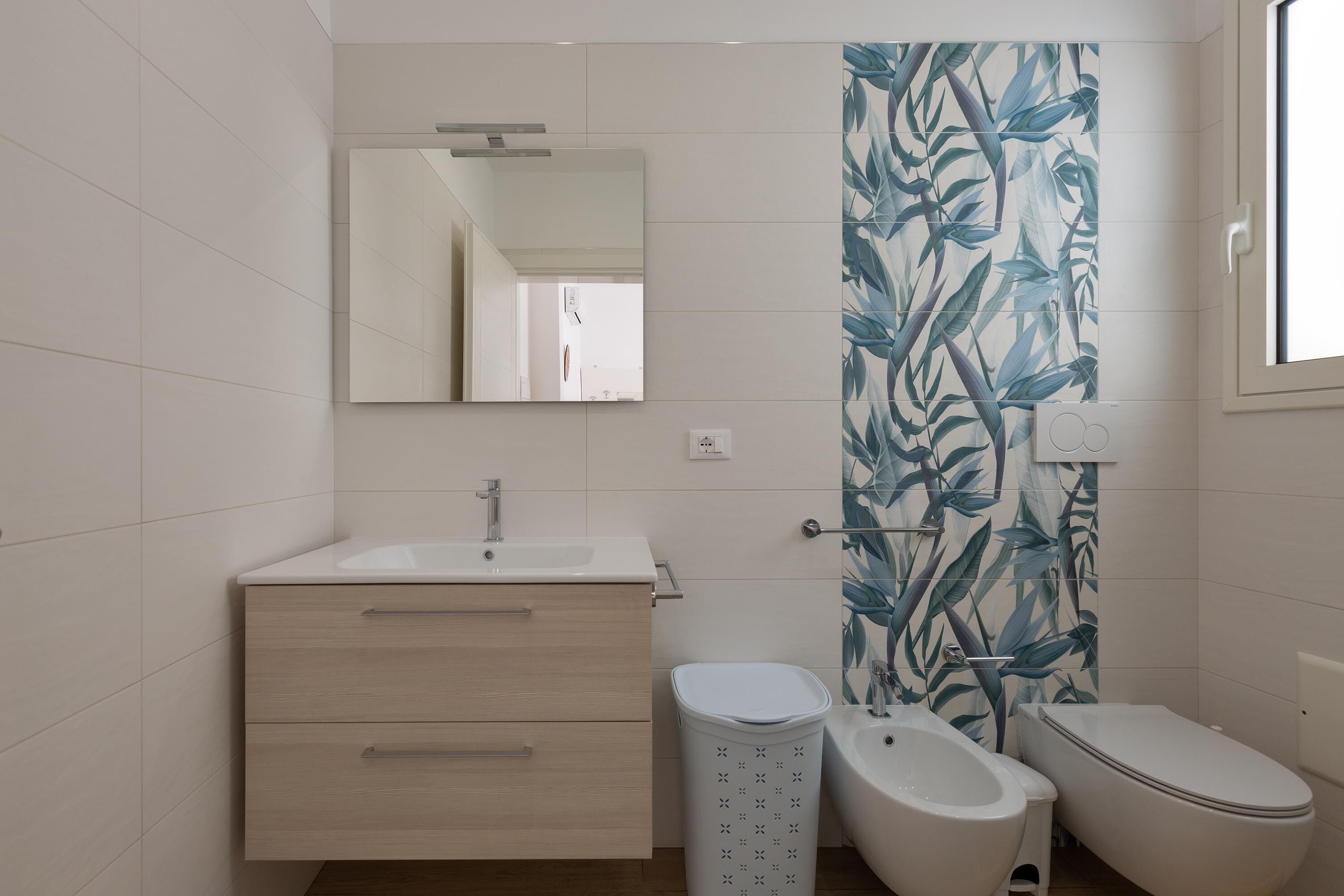 A modern bathroom with a white sink, mirror, and two toilets.