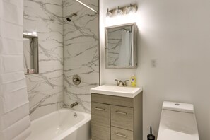 Ein Badezimmer mit Marmor-Duschwand, einer Badewanne, einem Waschbecken mit Spiegel darüber und einer Toilette.