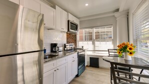 A kitchen with white cabinets, stainless steel appliances, a brick backsplash, and a dining area with a table and chairs. - Chic Newark Vacation Rental: 3 Mi to Airport! (Newark)