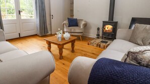 A cozy living room with a fireplace, a sofa, a coffee table, and a chair. - Mountfield Farm Cottage (Ashford)