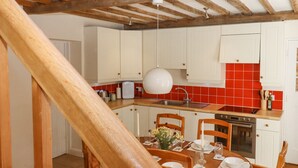 A kitchen with white cabinets, a red backsplash, and wooden beams. - Mountfield Farm Cottage (Ashford)