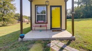 A covered porch with a bench, a yellow door, and a window.