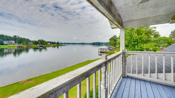 Blick auf das Wasser von einer überdachten Terrasse mit Geländer, mit Blick auf einen ruhigen See und entfernte Gebäude.