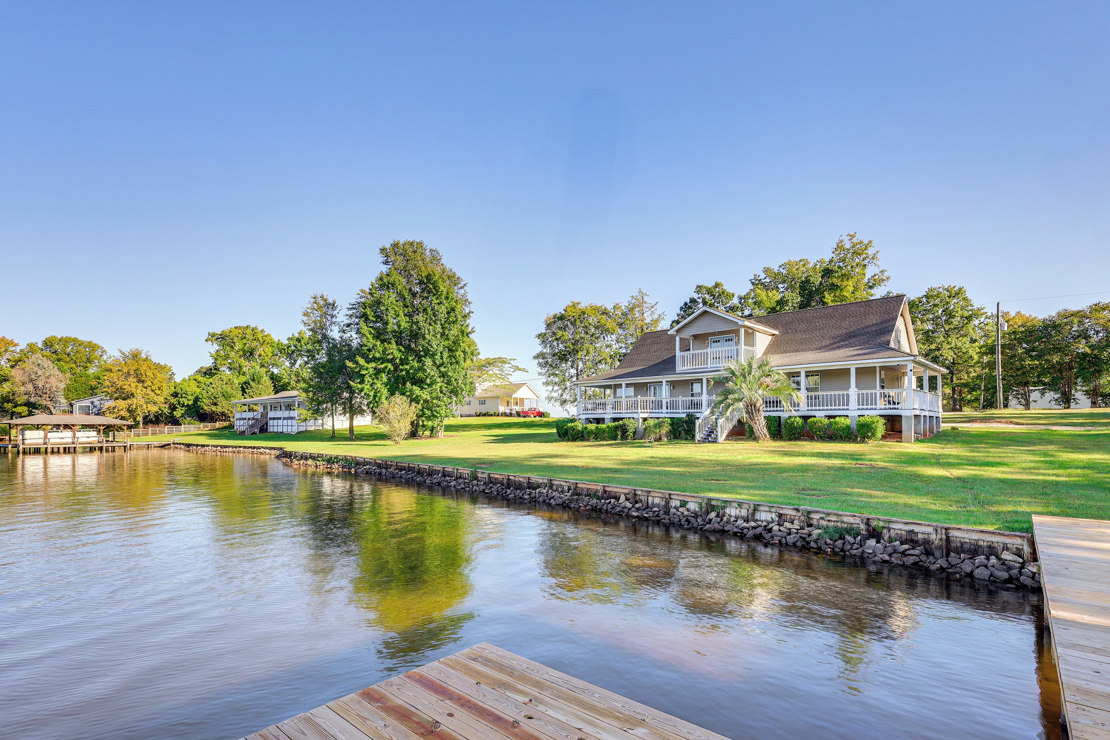 A lakeside property with a dock, a large house with a porch, and a well-maintained lawn.